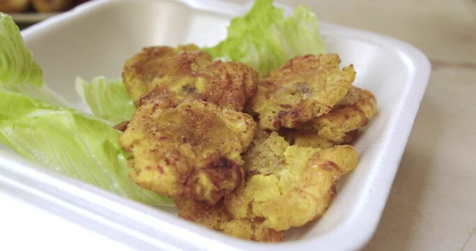 Primer plano de plato peruano de la selva con patacones o tostones siendo colocados en un recipiente.
