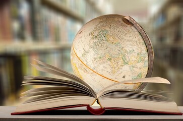 Old globe lying on an open book against the background of bookshelves in a library. Science,...