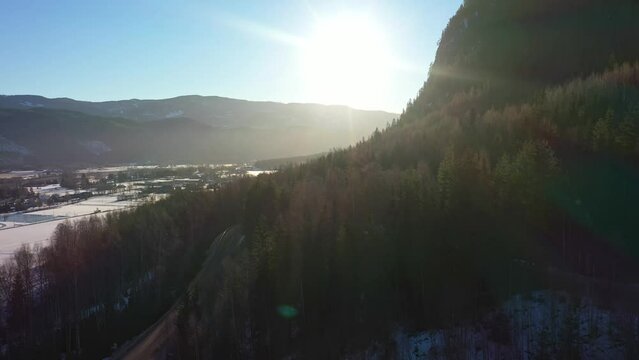 Spectacular winter sunrise above dark green forest in Nesbyen Hallingdal Norway - Backward moving aerial close to mountain while looking towards bright sun
