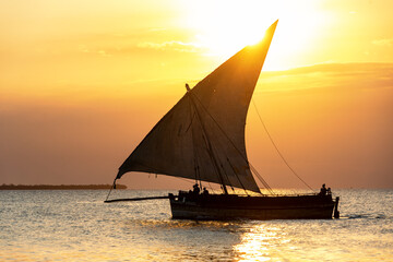 Fototapeta premium traditional sailing dhow heading out to sea at dusk on a calm evening ocean