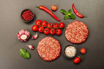 Raw steak cutlets from minced beef meat on black stone background. Fresh vegetables, mint