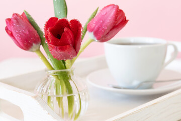 Tulips in glass vase and cup of coffee or tea on white wooden tray Close-up