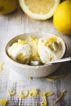bol con helado de limón que está siendo comido, sobre una tabla de madera blanca y con limones detrás 