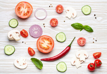 Food cooking background: arranged fresh ingredients, basil, cherry tomatoes, mushrooms, cut cucumber, onion, chilli pepper, spices on white wooden background top view