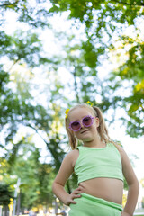 little model girl posing at the camera in sunglasses, holding her hand on her hips