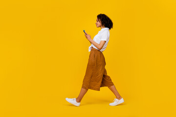Full length profile portrait of pretty nice lady walk hold use telephone chatting isolated on yellow color background