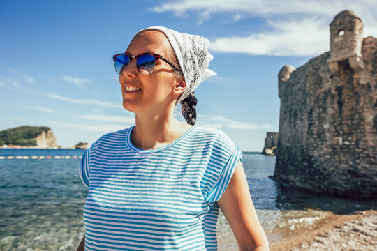 Mature woman in scarf on head walking along seaside promenade of old tourist town