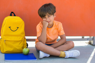 Fototapeta premium Little boy smiling on the first day of school. Little boy with yellow backpack and orange background. Back to school. Lifestyle