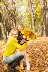 Happy family portrait, blonde mother and daughter in autumn forest, girl with leaves bouquet