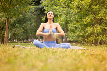 Slim girl meditating sitting in a lotus pose with closed eyes on the lawn in a park