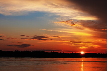 Sunset over the river. The sun sets below the horizon. Forest in the distance