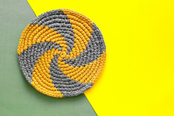 Grey yellow round spiral cup coaster on a yellow green background. Crochet stand for hot. Kitchen tools and accessories. Modern handmade concept. Copy space. Top view. - obrazy, fototapety, plakaty