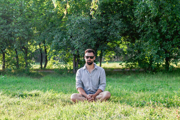 Naklejka na ściany i meble Young handsome European man in casual clothing and sunglasses sitting on a grass in summer park. 