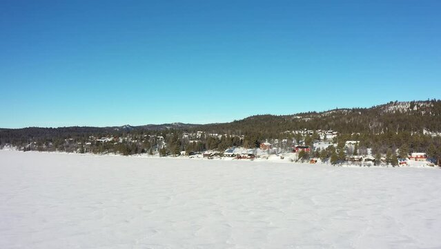 Ice covered synstevatn in Nesfjellet mountain close to Nesbyen Norway - Beautiful morning aerial flying above snow and ice covered freshwater lake towards leisure homes and road Rukkedalsvegen