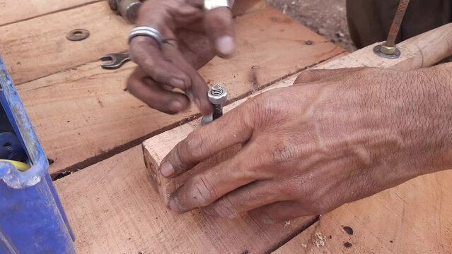 Kart Painter is fixing the handle of the wooden thela gaadi by hand with a nut bolt