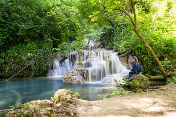 Amazing landscape with a girl enjoys a beautiful waterfall in green spring forest, Krushuna falls, Balkan Mountains, Bulgaria