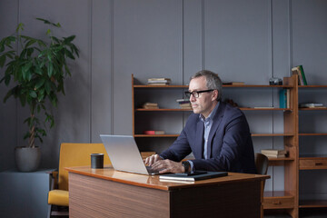 Serious pensive thoughtful focused business accountant bookkeeper in office looking at and working with laptop and income tax
