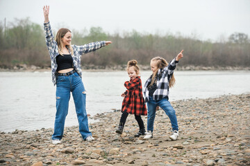 mother with two daughters on an active and fun walk outside the city near the river, they dance and whirl together