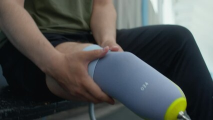 Close up tilt up shot of professional runner with amputated leg putting prosthetic sock on socket white getting ready for exercising at indoor stadium - Powered by Adobe