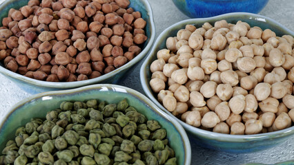 Assortment of dry chickpea piles in bowls. Three different chick pea kinds: green, kala chana and white.