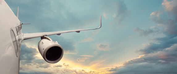 Commercial plane flies in the sky against the sun light and clouds.