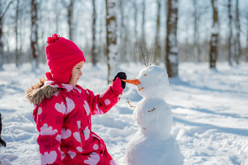 Little girl building snowman in snowy park. Active outdoors leisure with family with children in...