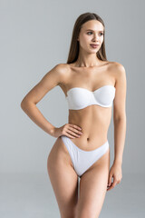 Young pretty woman with perfect slim body. Beautiful woman wearing inner wear, smiling and posing on grey background.