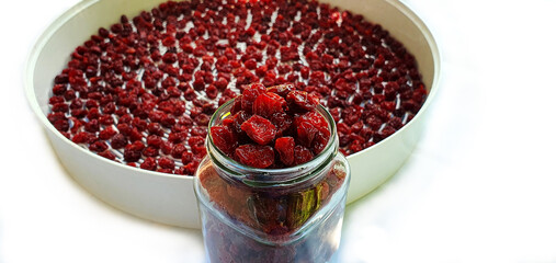 Homemade dried cherries stacked in a jar close-up isolated. In the background, a new portion of red delicious pitted cherries continues to dry