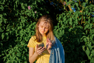 teenage girl in a yellow dress listens to music and holds a phone in her hands