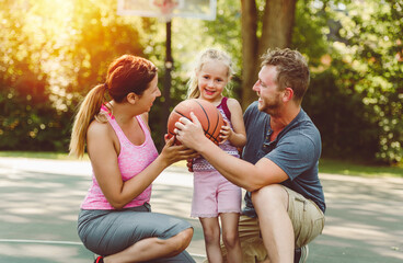 Happy family and child daughter outside at basketball court.