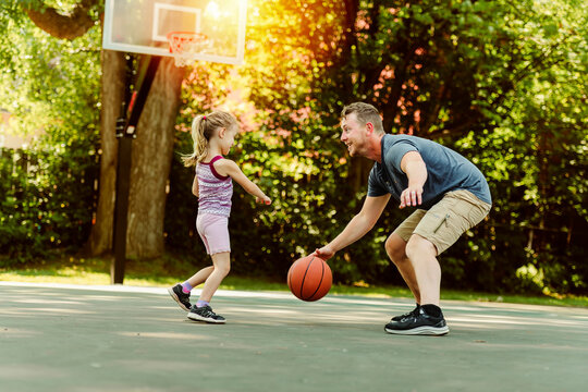 Happy father and child daughter outside at basketball court.