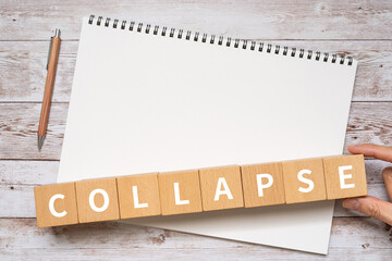 崩壊のイメージ｜「COLLAPSE」と書かれたブロック、ノート、ペン、手
