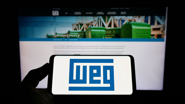 Stuttgart, Germany - 07-23-2022: Person holding mobile phone with logo of Brazilian company WEG Equipamentos Eletricos S.A. on screen in front of web page. Focus on phone display.