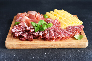 Fototapeta na wymiar Cheese, prosciutto, salami on a wooden square board on a black stone background. Delicacy.