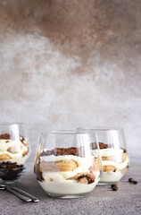 Classic tiramisu with savoiardi in a glass on a brown stone background