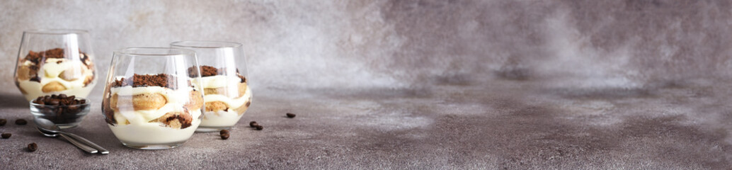Classic tiramisu with savoiardi in a glass on a brown stone background
