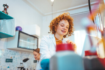 Beautiful Female Scientist Wearing Protective Goggles Mixing Chemicals in a Test Tube in a Lab. Young Professional Microbiologist Working in Modern Laboratory with Technological Equipment.