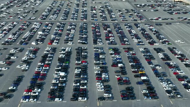 High aerial pull back and tilt up revealing sprawling parking lot at Manheim Auto Auction. Thousands of new and used cars for wholesale to dealers on auction.
