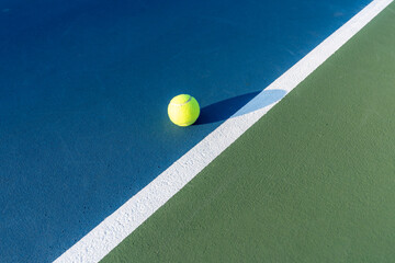 Yellow tennis ball at blue tennis court with white baseline and green out of bounds	