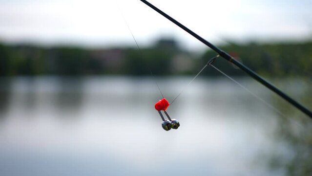 Fishing rod sinker on equipment outdoors at background of river water. Side view fishing tool on summer sunrise on lake shore. Hobbies and relaxation concept