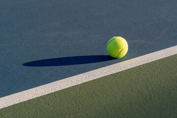 Yellow tennis ball at blue tennis court with white baseline and green out of bounds	