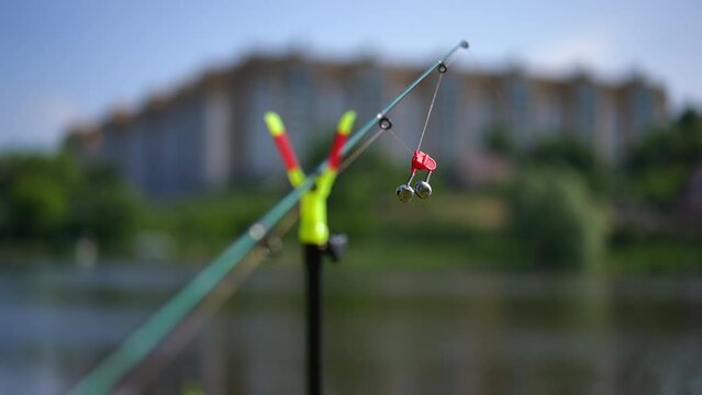 Close-up fishing sinker on fishing pole outdoors in urban park with blurred city at background. Fishing rod on sunny summer morning at background of river water. Leisure and hobbies concept