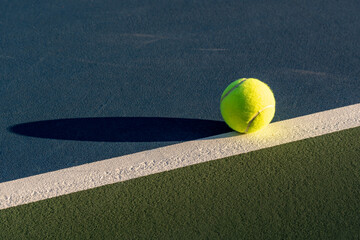 Yellow tennis ball at blue tennis court with white baseline and green out of bounds	