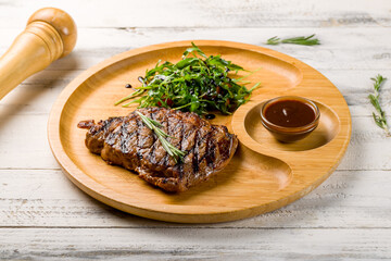 juicy Ribeye steak on wooden plate with aragula, tomatoes and pepper sauce