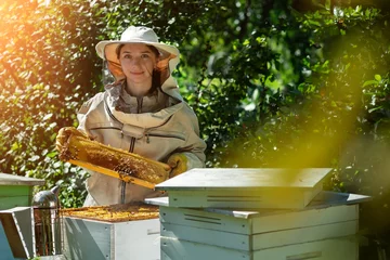 Fotobehang Young female beekeeper hold wooden frame with honeycomb. Collect honey. Beekeeper on apiary. Beekeeping concept. © kosolovskyy