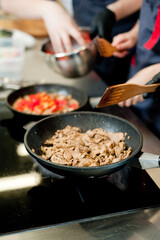 Cook fries meat in a pan with vegetables.