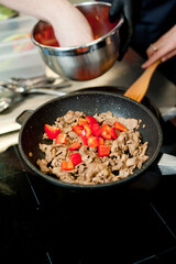 Cook fries meat in a pan with vegetables.
