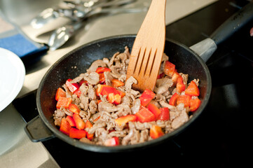 Cook fries meat in a pan with vegetables.