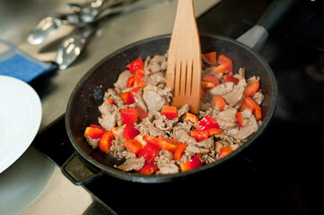 Cook fries meat in a pan with vegetables.