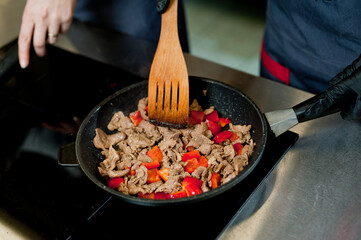 Cook fries meat in a pan with vegetables.